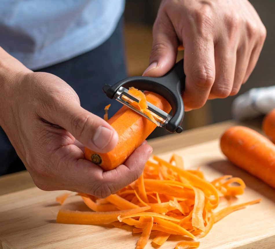 Personne épluchant une carotte sur une planche.