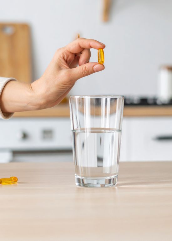 Main tenant une gélule au-dessus d'un verre d'eau.