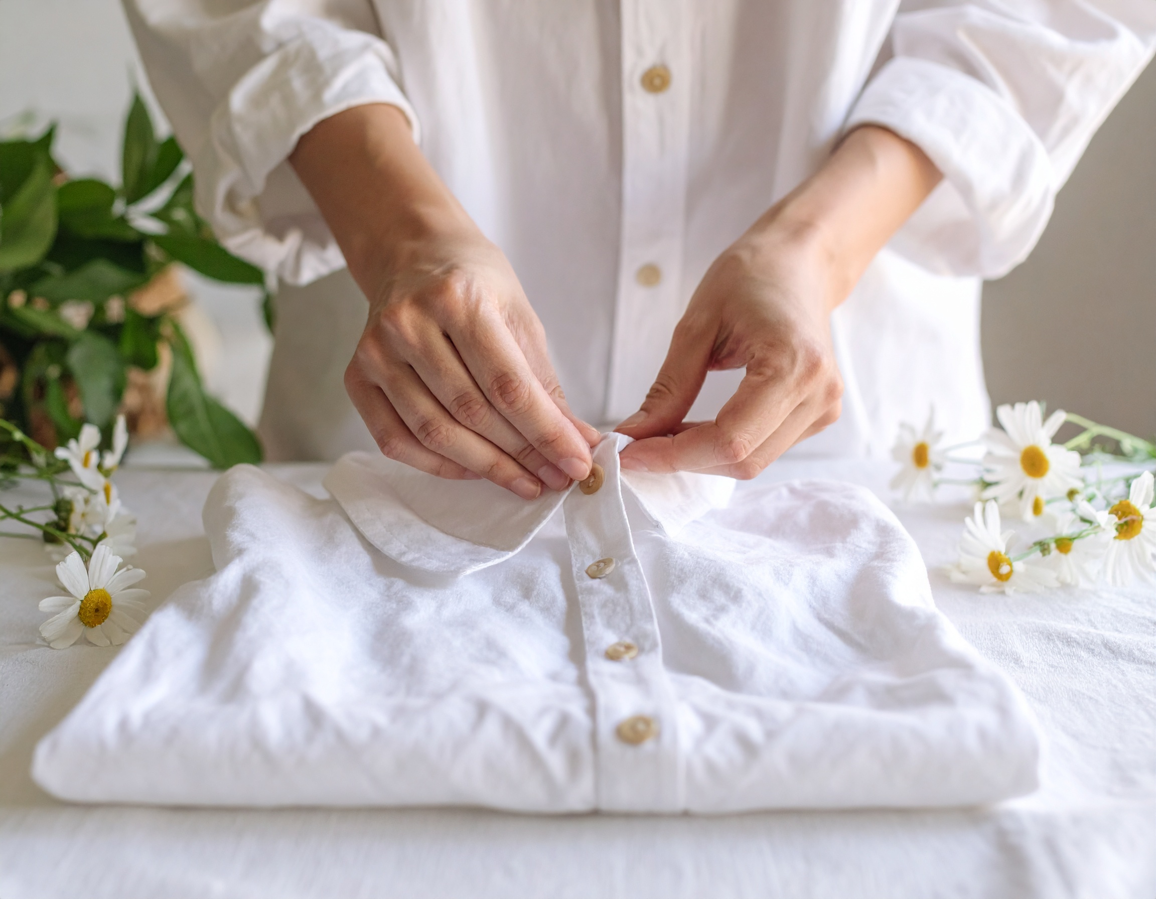 Femme plie une chemise blanche avec des fleurs.