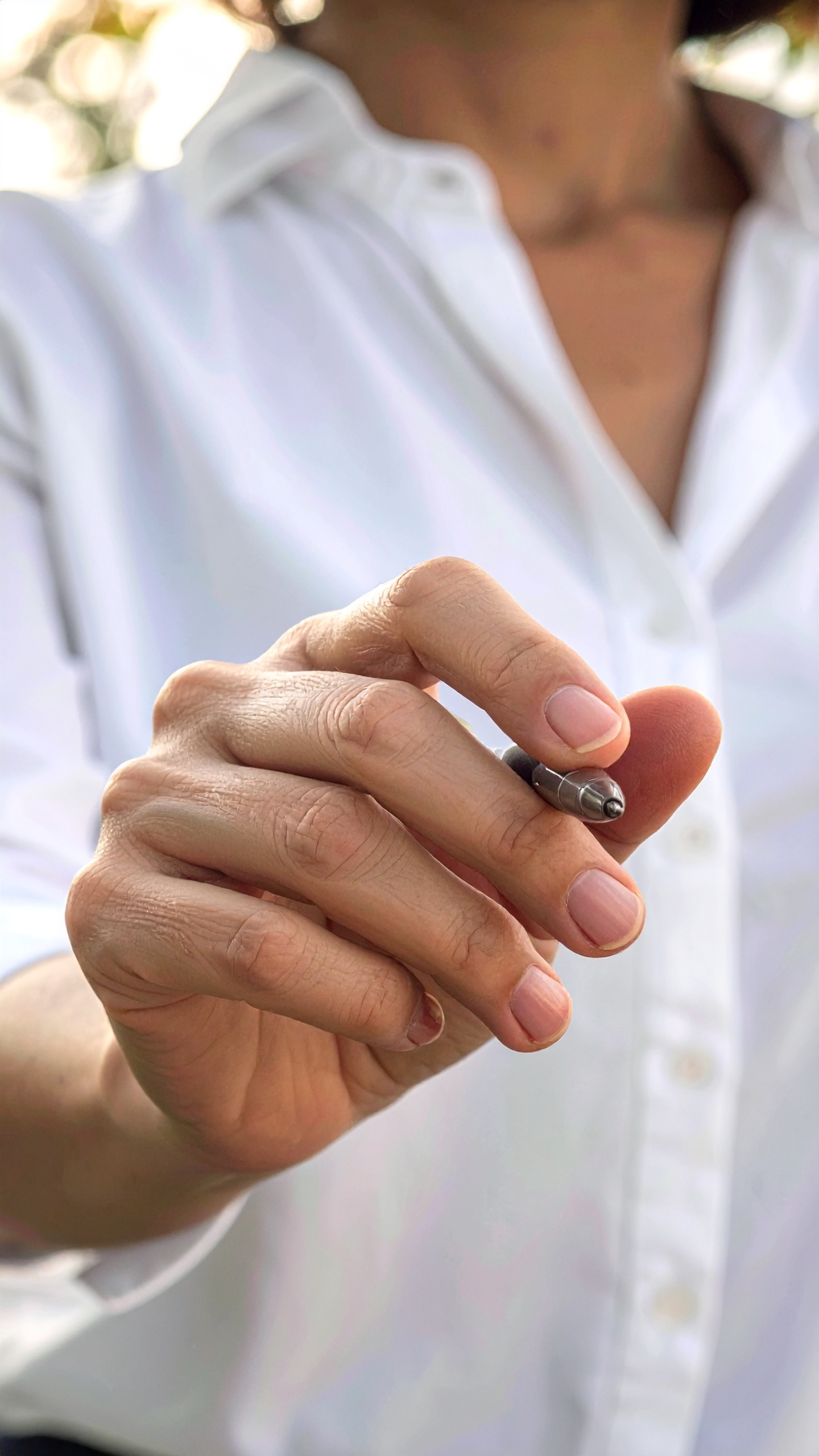 Main tenant un stylo, fond flou naturel.