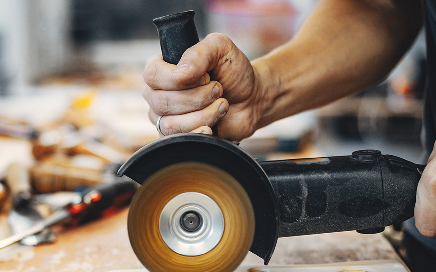 Main utilisant une meuleuse sur du bois.