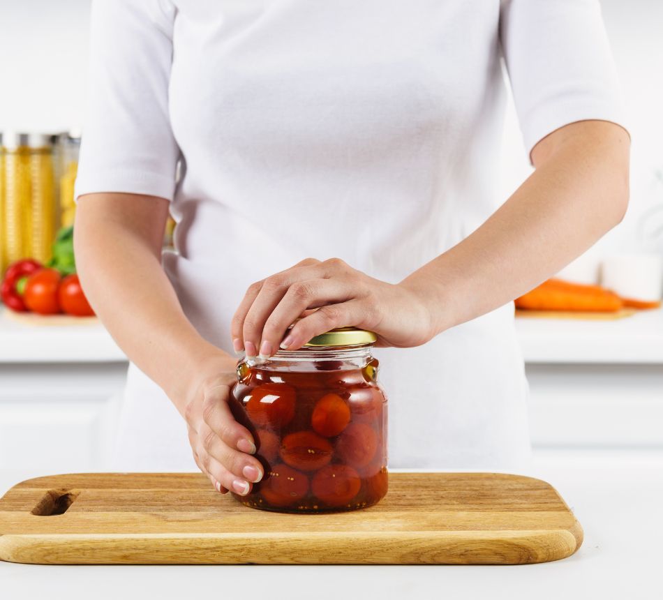 Vrouw opent een pot met tomaten in keuken.